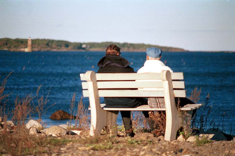 Lighthouse across the bay, people on bench in foreground (56K)